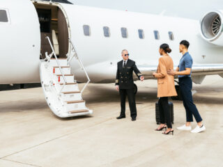 Passengers boarding in private luxury jet near hangar, pilot welcomes the young successful passengers - Journey House Travel