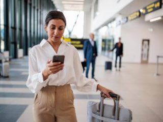 Businesswoman using a smartphone in an airport terminal - Journey House Travel