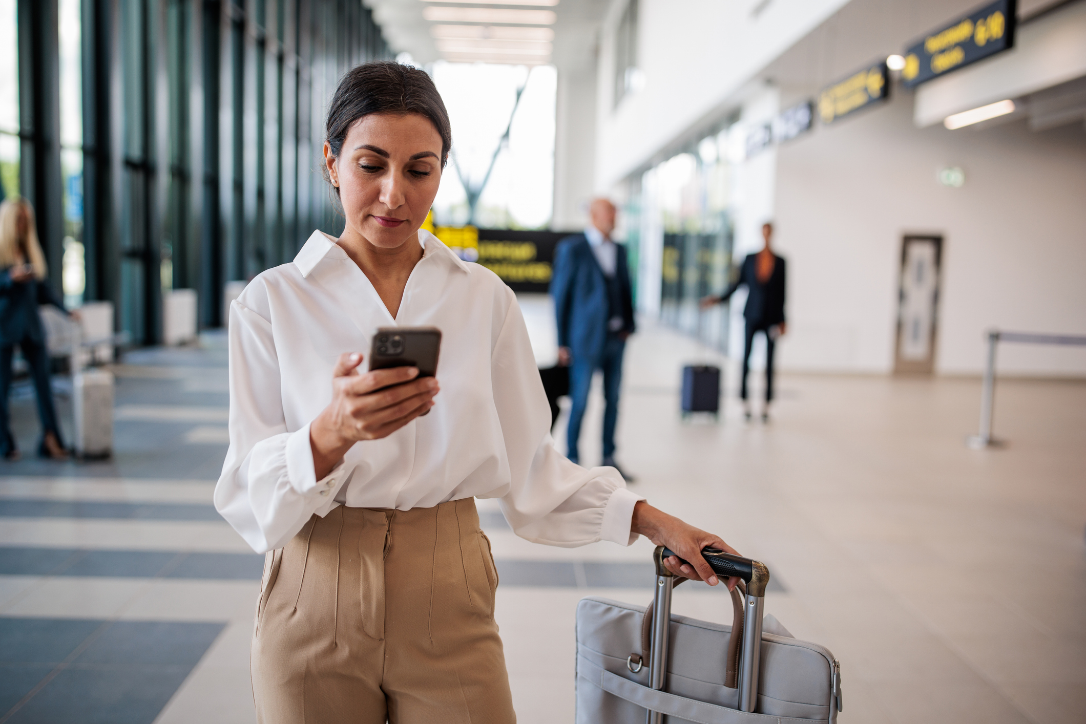 Businesswoman using a smartphone in an airport terminal - Journey House Travel